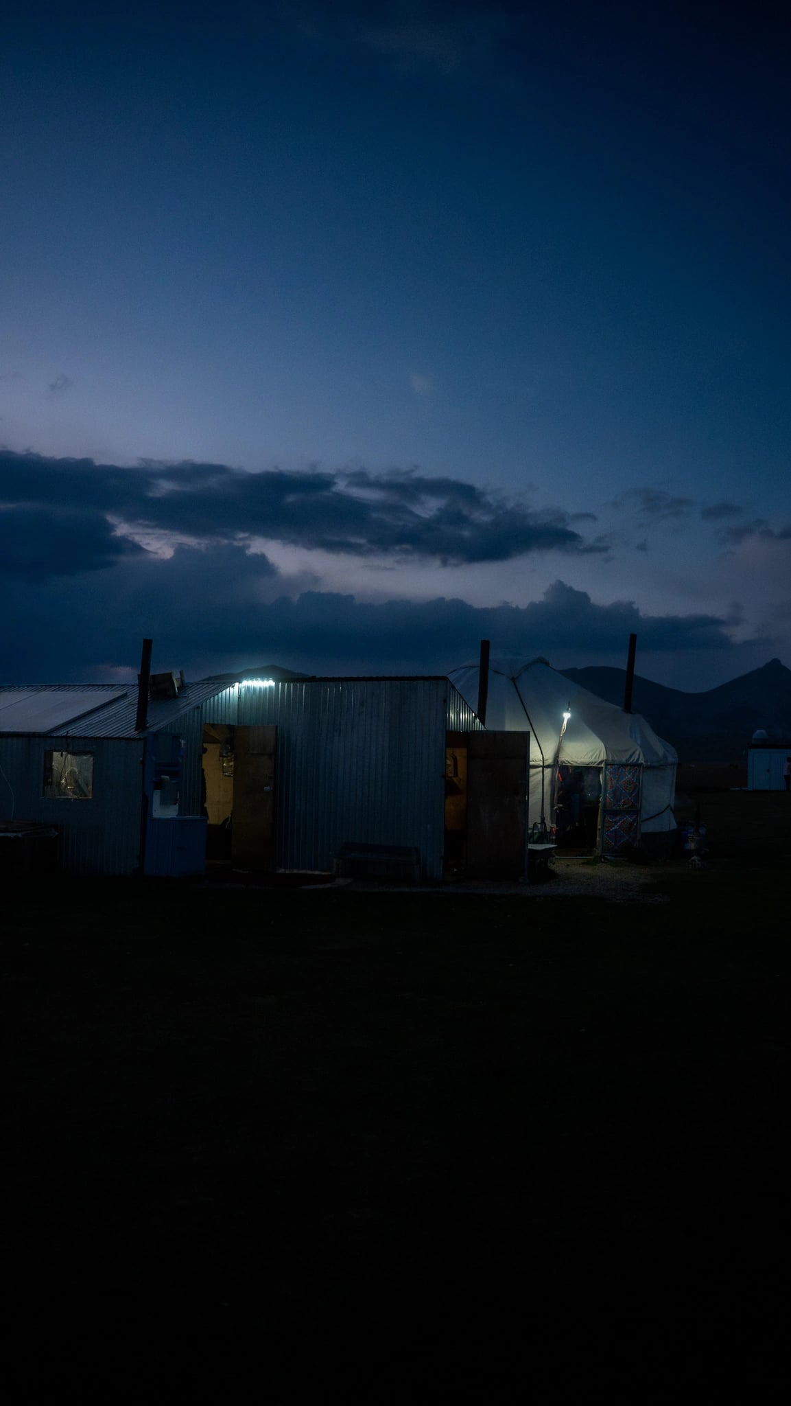 Yurt en eenvoudig kampgebouw verlicht tijdens het blauwe uur bij Song-Kul